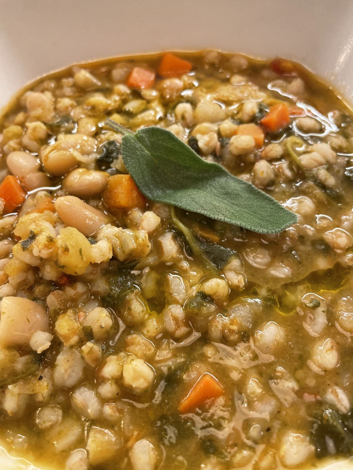 A bowl of bean and farro soup with vegetables and a sage leaf