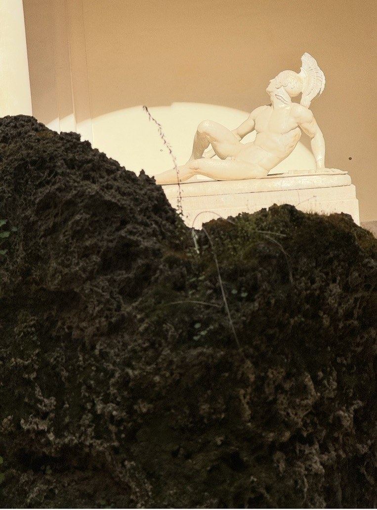 A white marble statue of a reclining warrior in a garden niche, lit by golden October sun