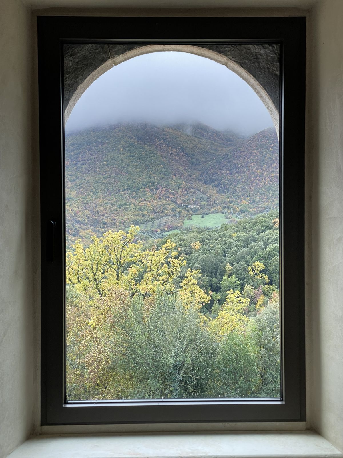 An arched window looking out over autumn woods and misty hills