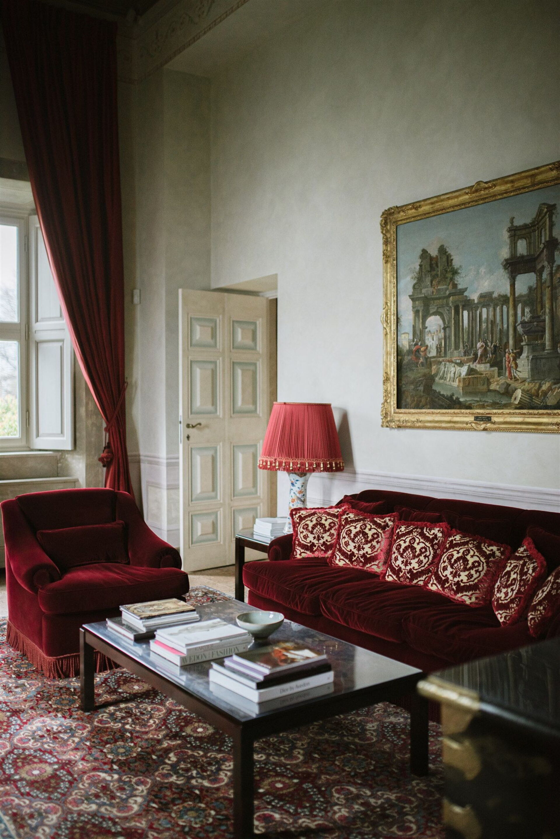 Villa Balbiano master suite living room with crimson velvet sofa, ruby curtains, and a baroque painting of Roman ruins