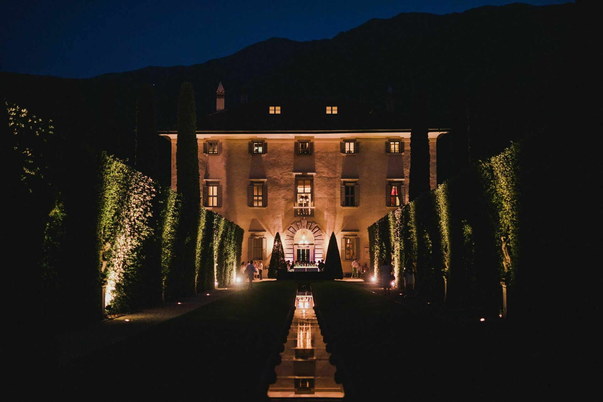 Villa Balbiano on Lake Como illuminated at night with cypress trees lining a reflecting pool