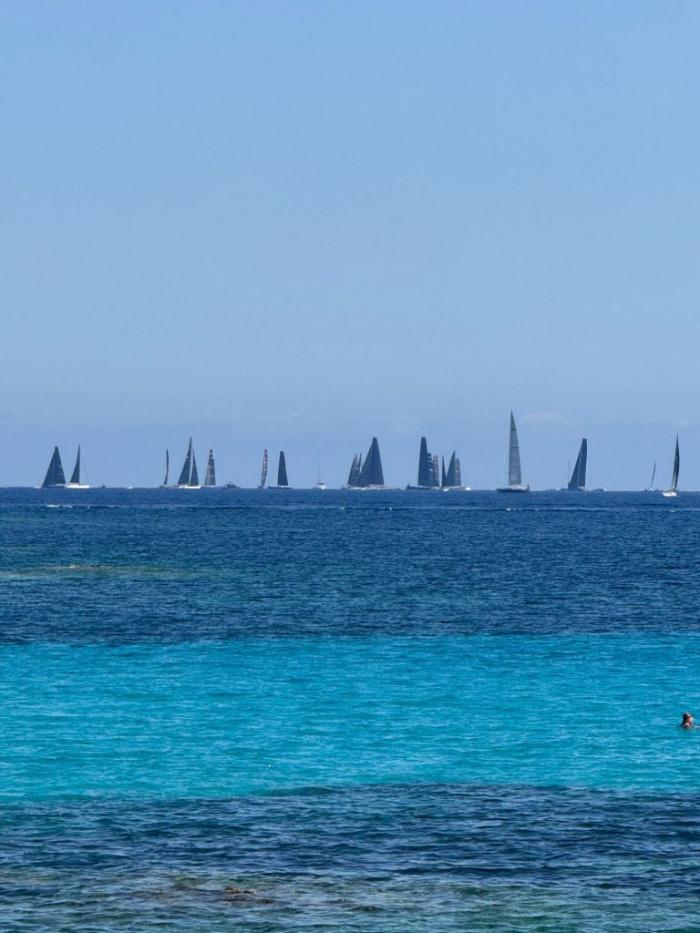 Maxi yachts racing on the horizon beyond turquoise water, Sardinia