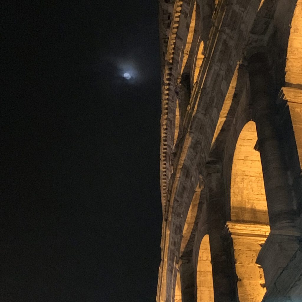 The arches of the Colosseum lit up at night under a full moon
