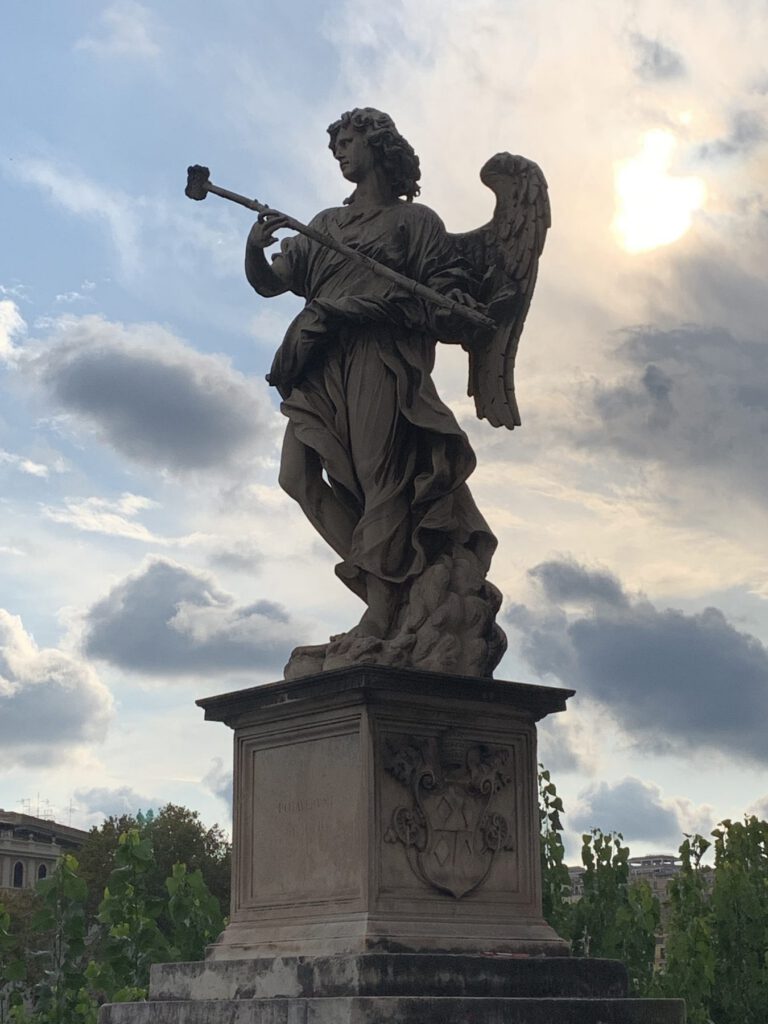 A Baroque angel statue on Ponte Sant'Angelo in Rome against a bright cloudy sky
