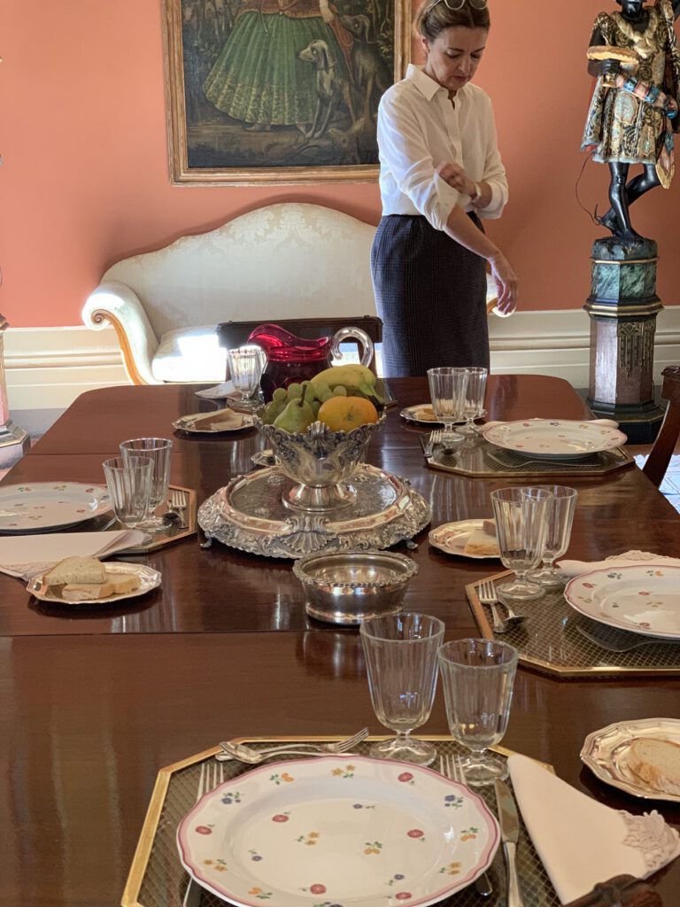 A long dining table set for dinner in a villa dining room with a painting on the wall
